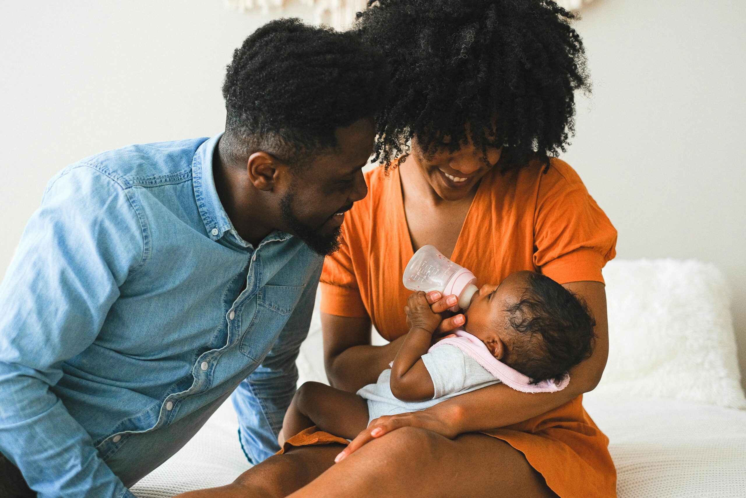 A joyful moment of parents feeding their baby using a bottle indoors.