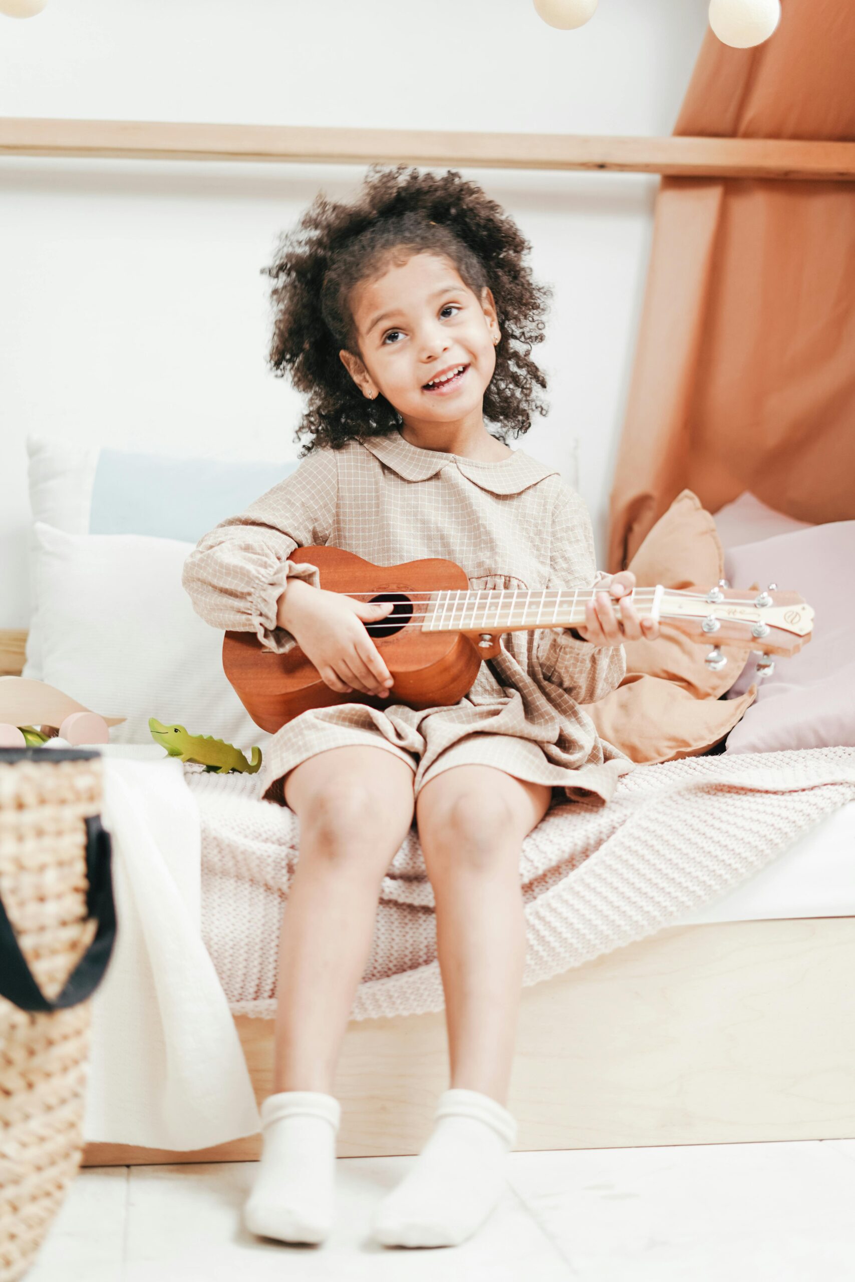 Joyful child with afro hair playing a ukulele indoors, capturing innocence and happiness.