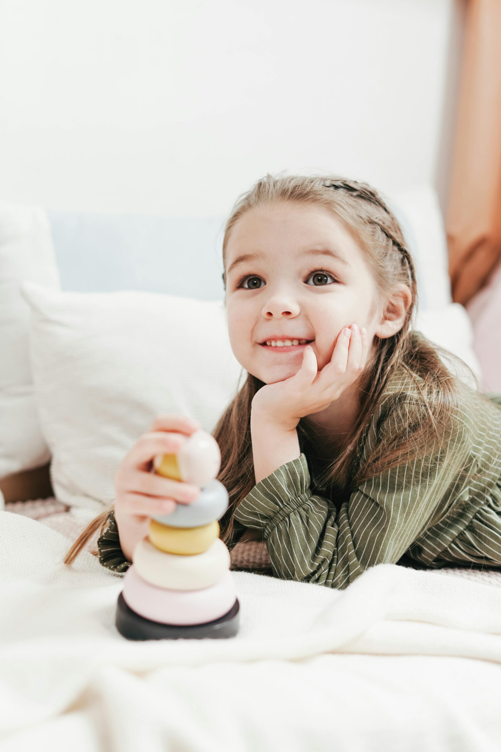 Adorable child playing happily with a stacking toy on the bed indoors.