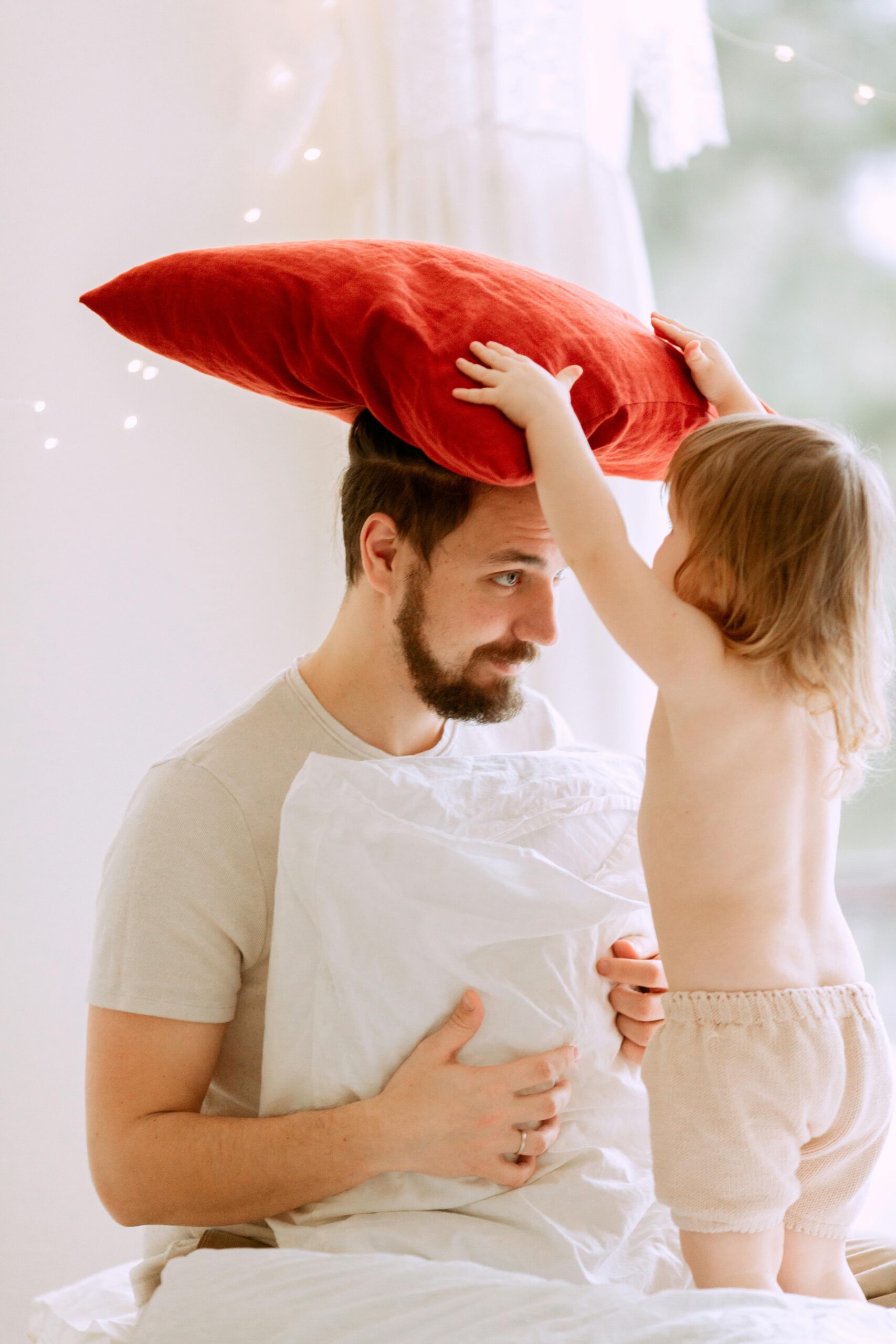 A joyful father and toddler play with pillows in a bright indoor setting, capturing a moment of bonding.