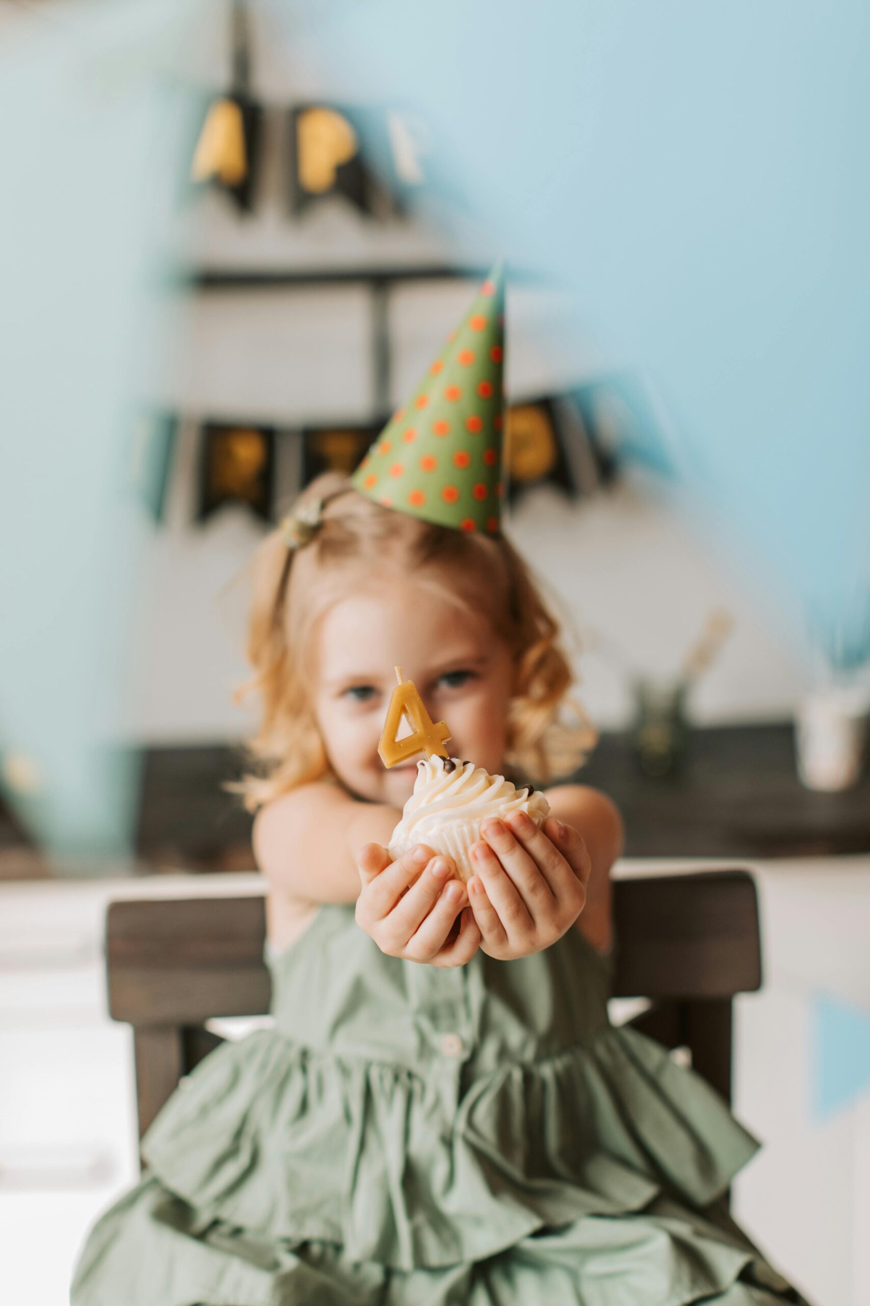 A cute child celebrates her fourth birthday with a cupcake and party hat indoors. Joyful birthday atmosphere.