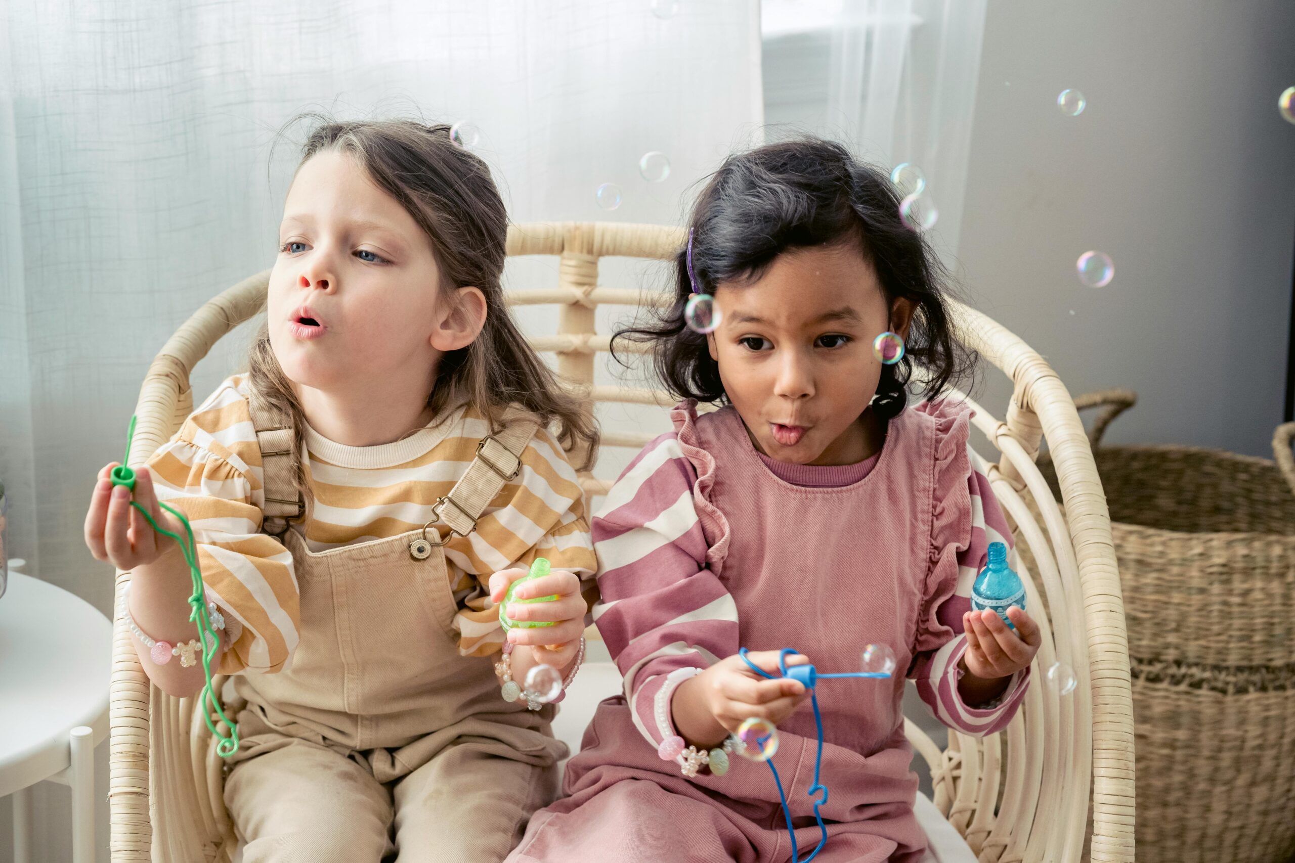 Two children joyfully blowing bubbles indoors, capturing childhood fun and innocence.