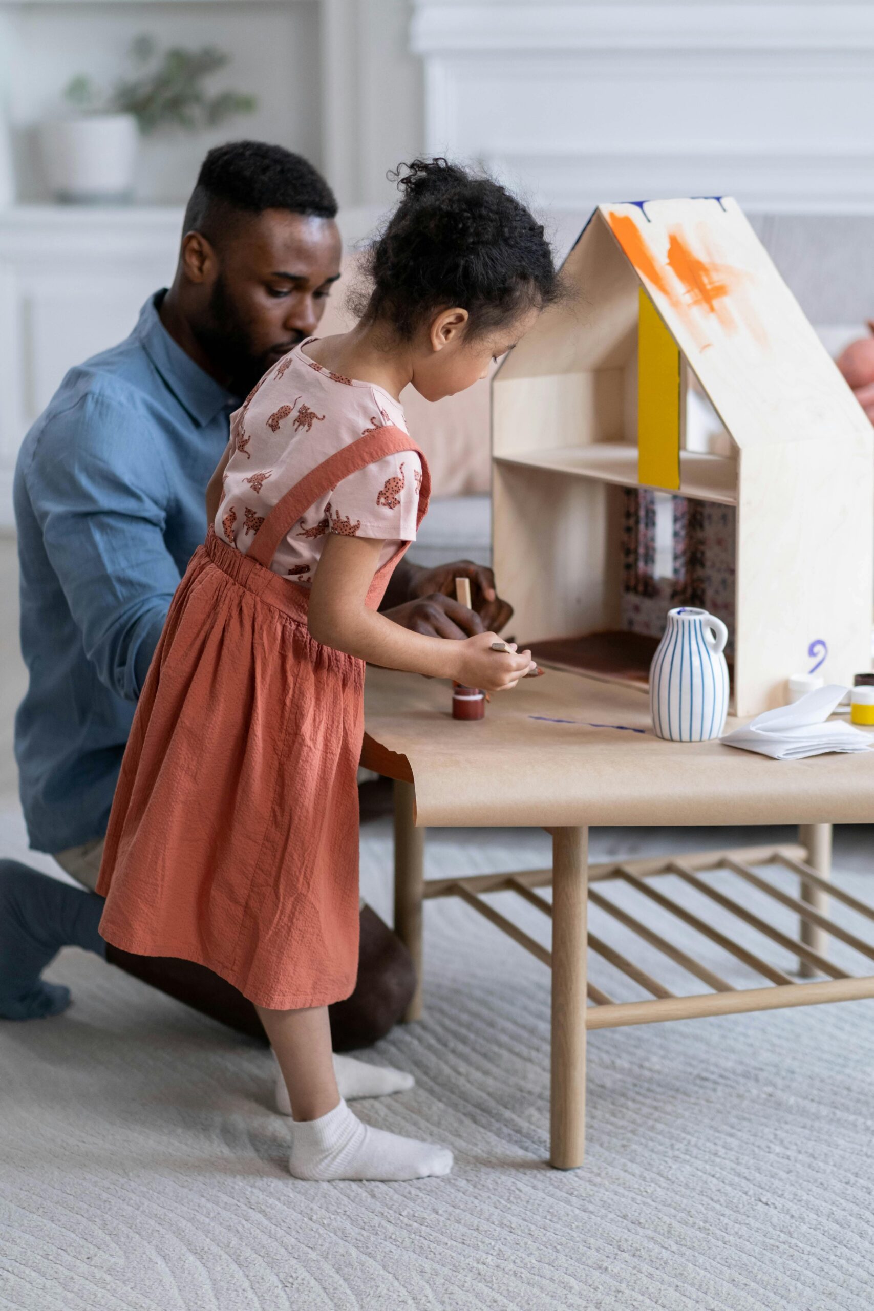 A father and daughter engage in play with a dollhouse in a cozy living room setting.